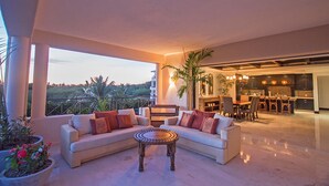 Amplia sala de estar con sofá y mesa de centro, un balcón con vistas y una cocina al fondo.