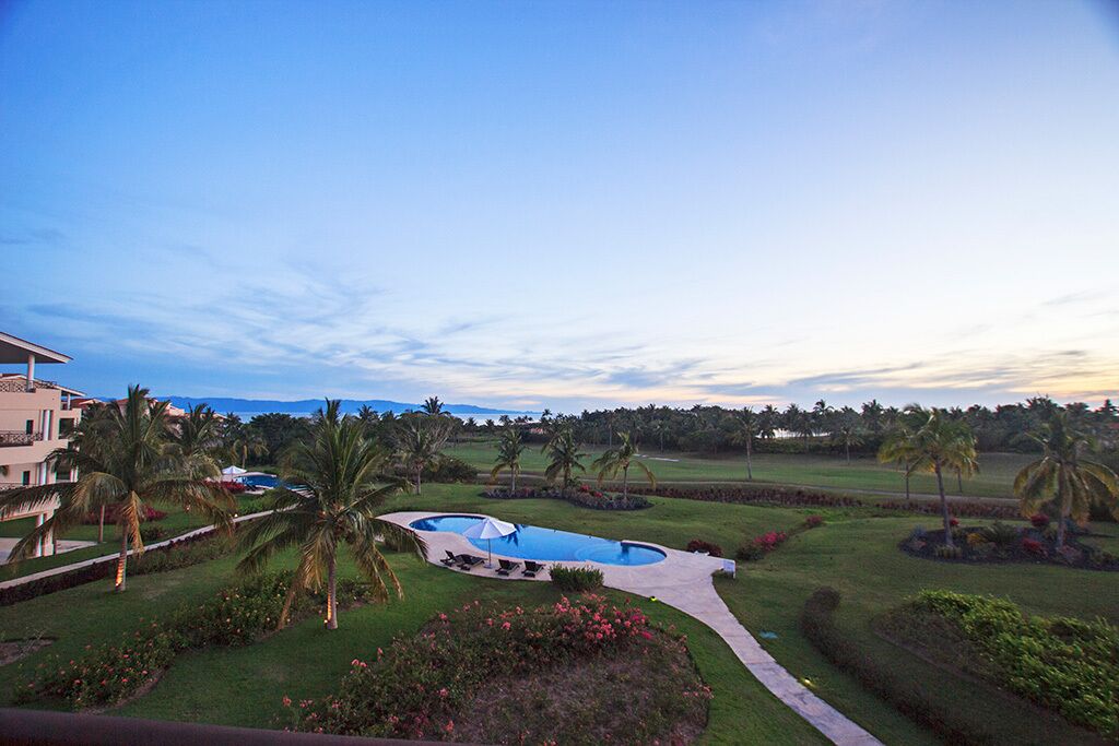 A golf course with a swimming pool, palm trees, and a building in the background.