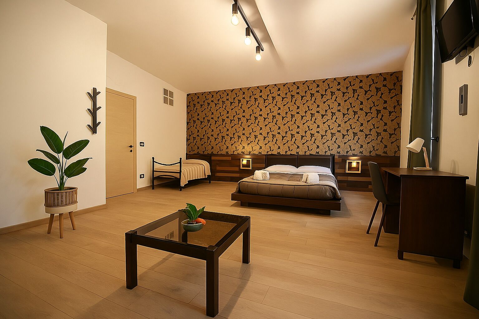 A bedroom with a bed, bedside tables, a desk, a chair, a small table with a plant, and a potted plant.
