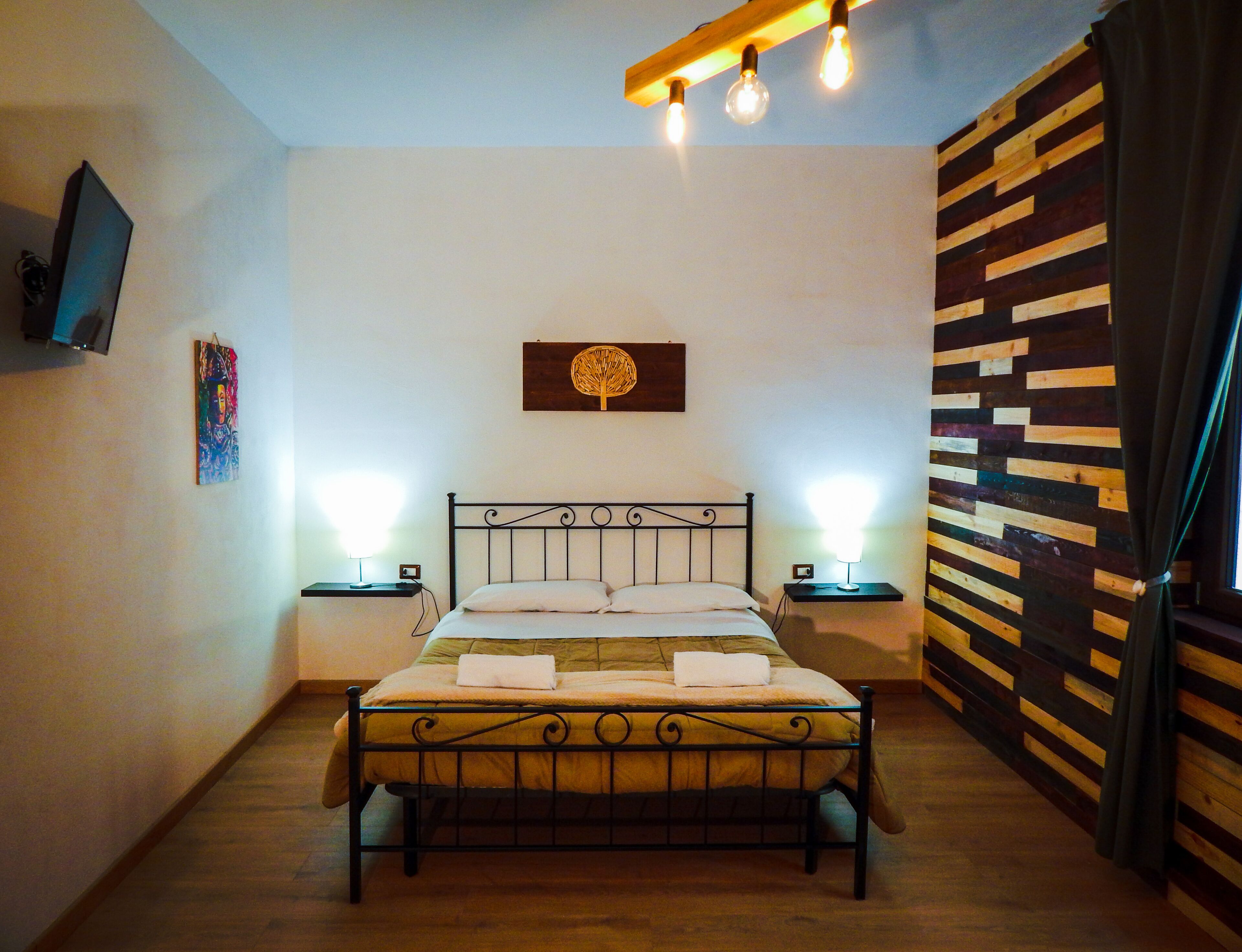 A bedroom with a bed, bedside lamps, a wall-mounted TV, and a wooden wall panel.