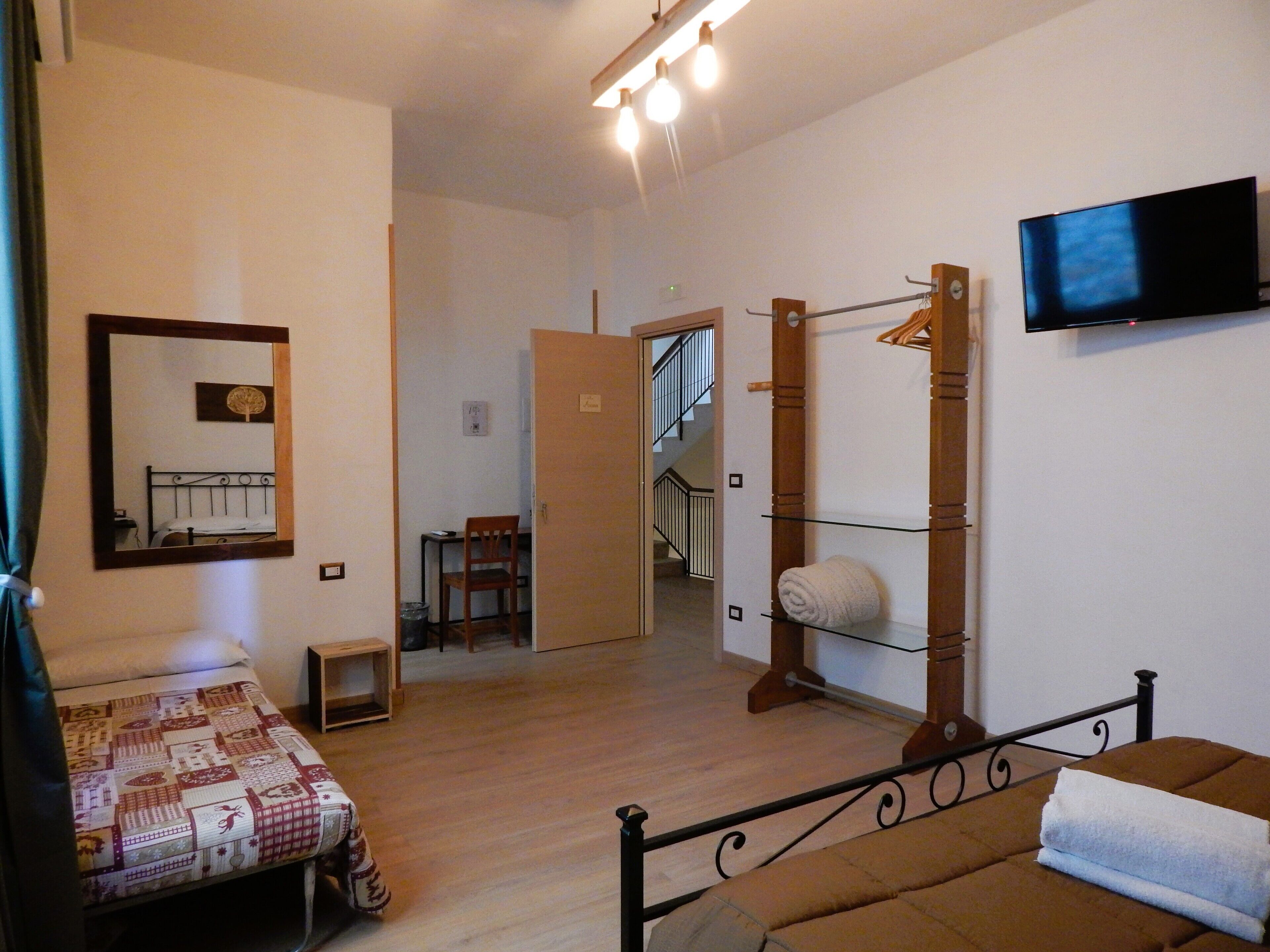 A bedroom with a bed, a chair, a small table, a mirror, a TV, and a staircase leading to another room.