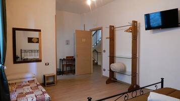 A bedroom with a bed, a chair, a small table, a mirror, a TV, and a staircase leading to another room.