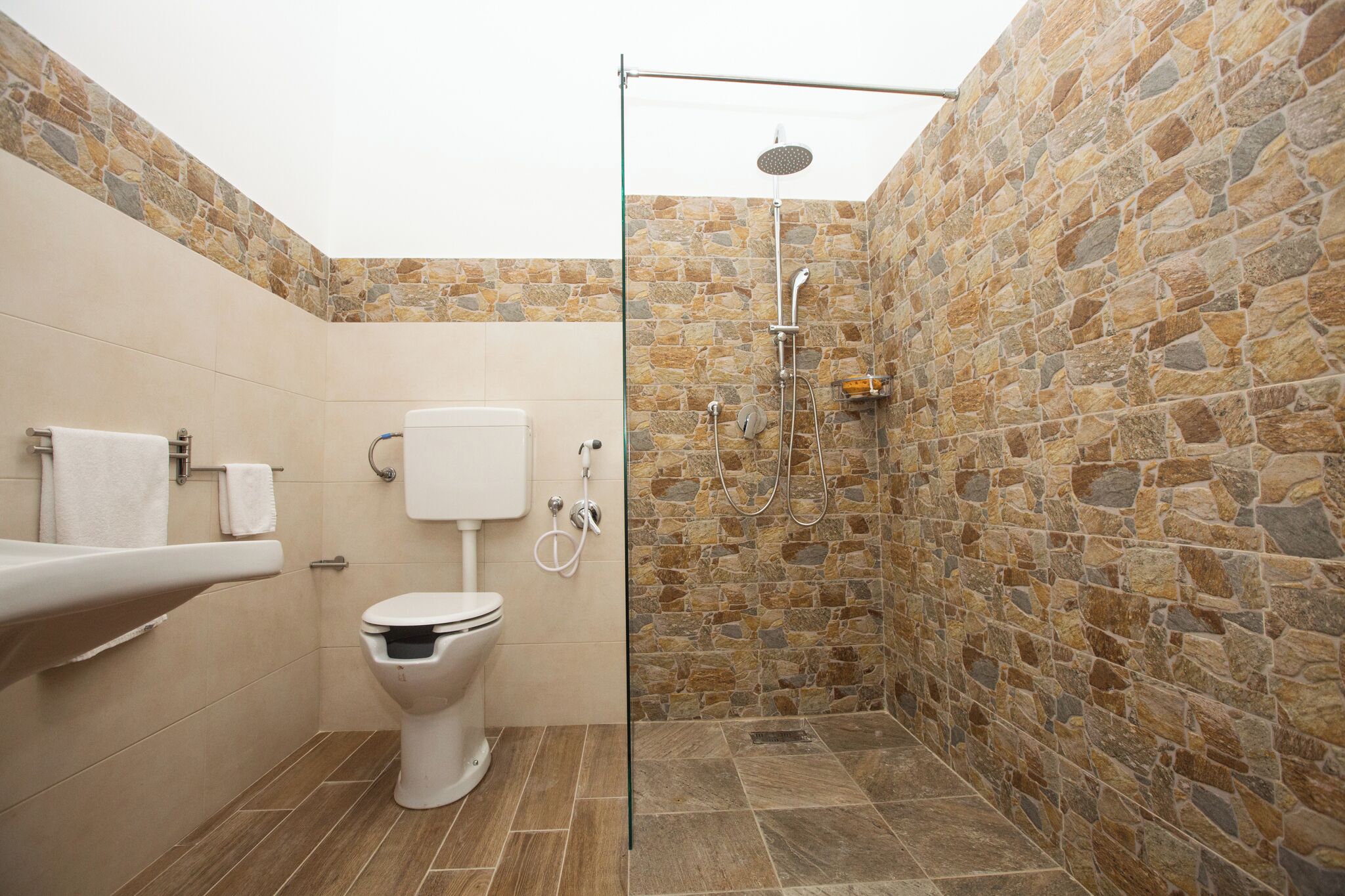 A bathroom with a stone wall shower, a toilet, and a sink.