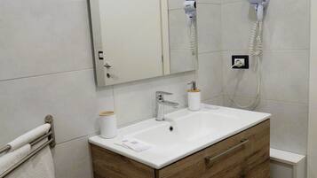 A bathroom with a wooden vanity, a white sink, a mirror, and a hairdryer mounted on the wall.