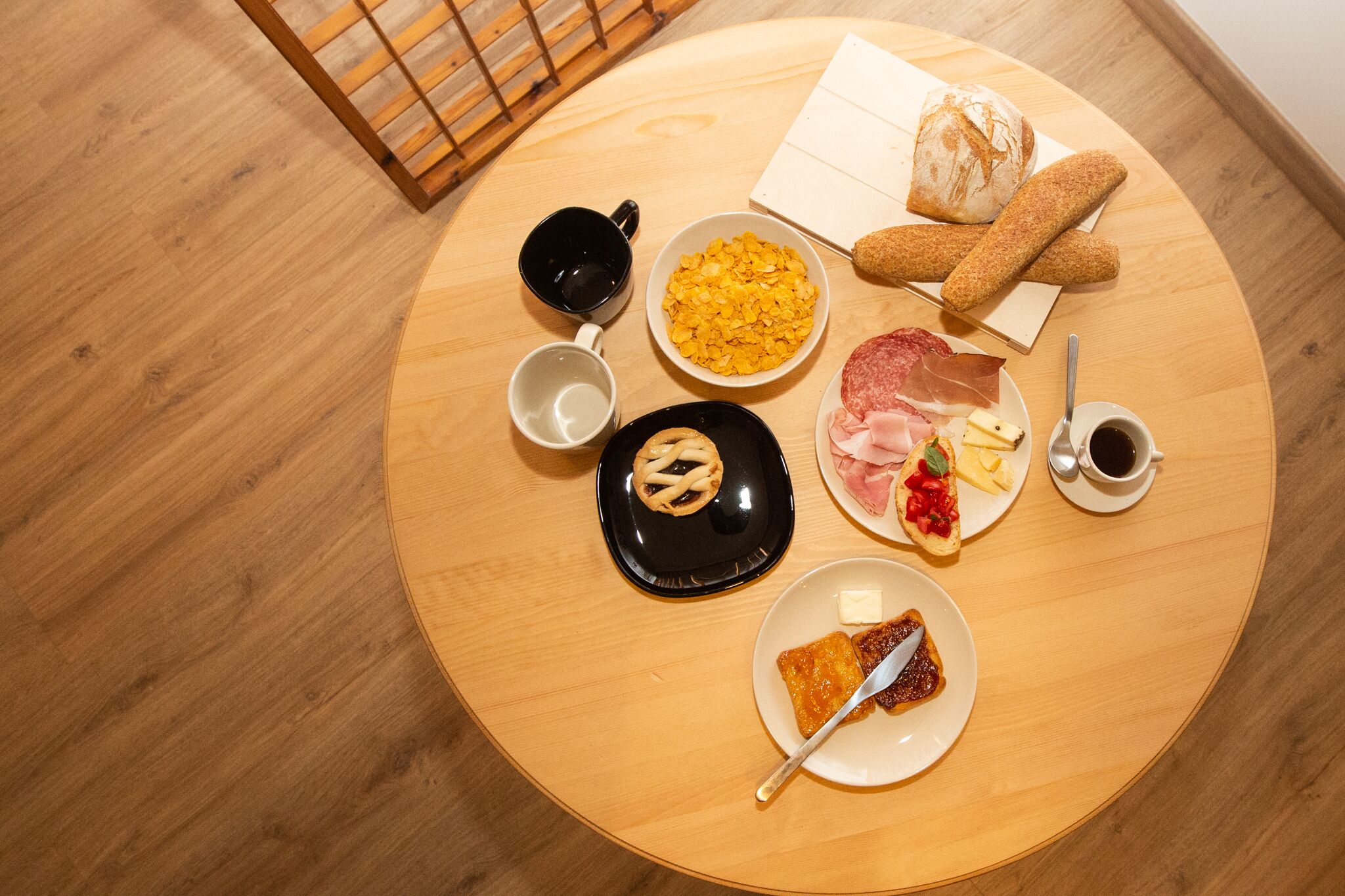 Une table ronde en bois, sur laquelle sont disposés divers aliments pour le petit-déjeuner, notamment du pain, du fromage, du jambon et un croissant.
