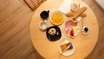 Taula rodona de fusta amb diversos aliments per esmorzar, com ara pa, formatge, pernil i un croissant.