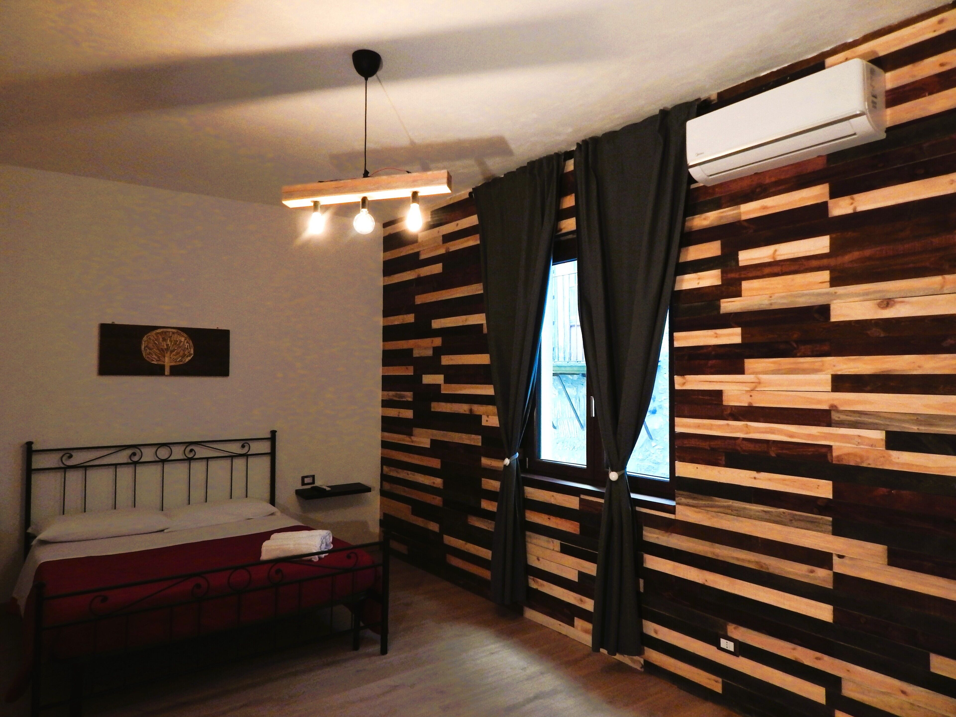 Un dormitorio con cama, lámpara colgante, ventana con cortinas y pared con diseño de paneles de madera.
