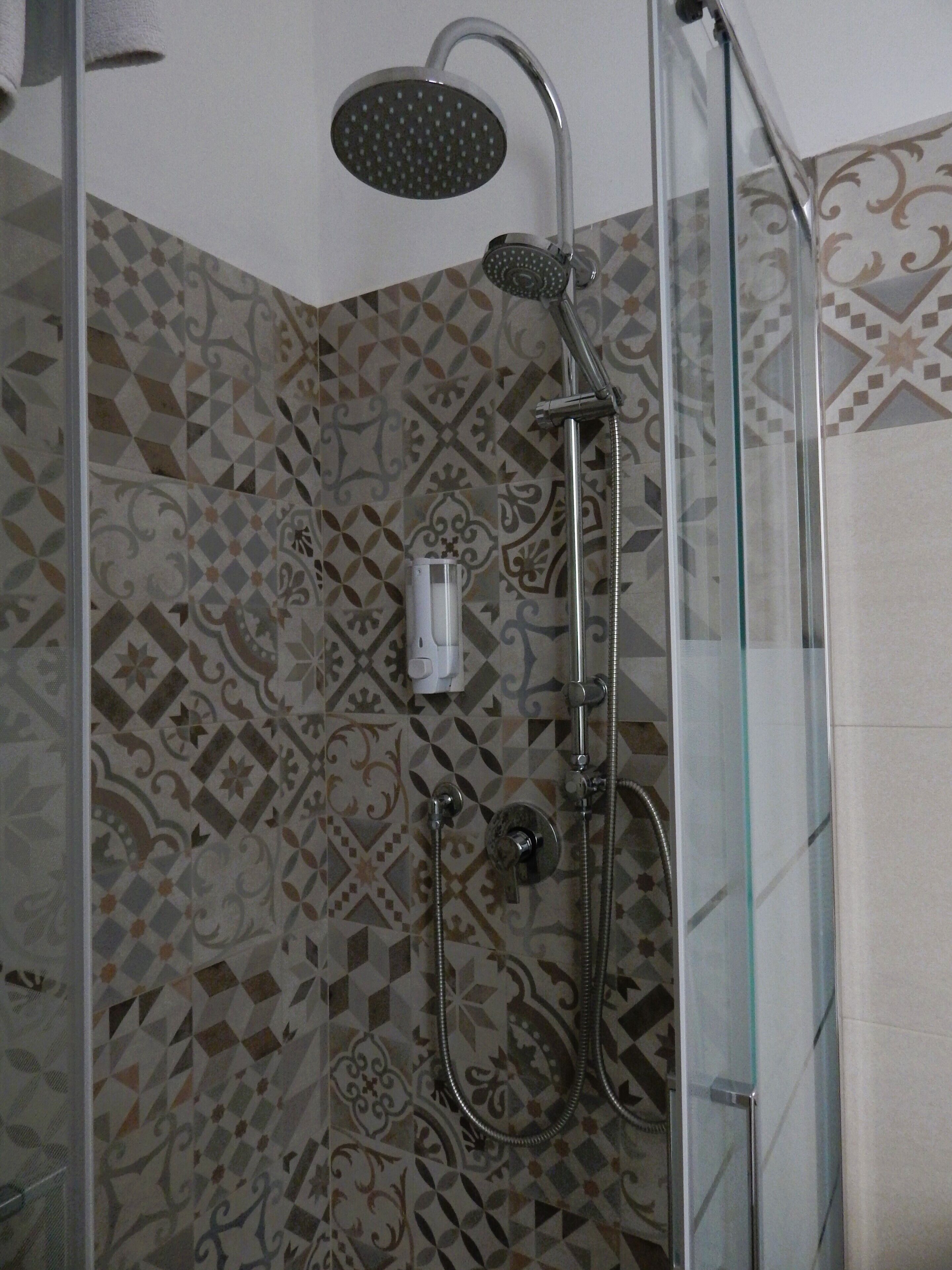 Ducha con cerramiento de vidrio, cabezal de ducha de mano y panel de control en la pared.