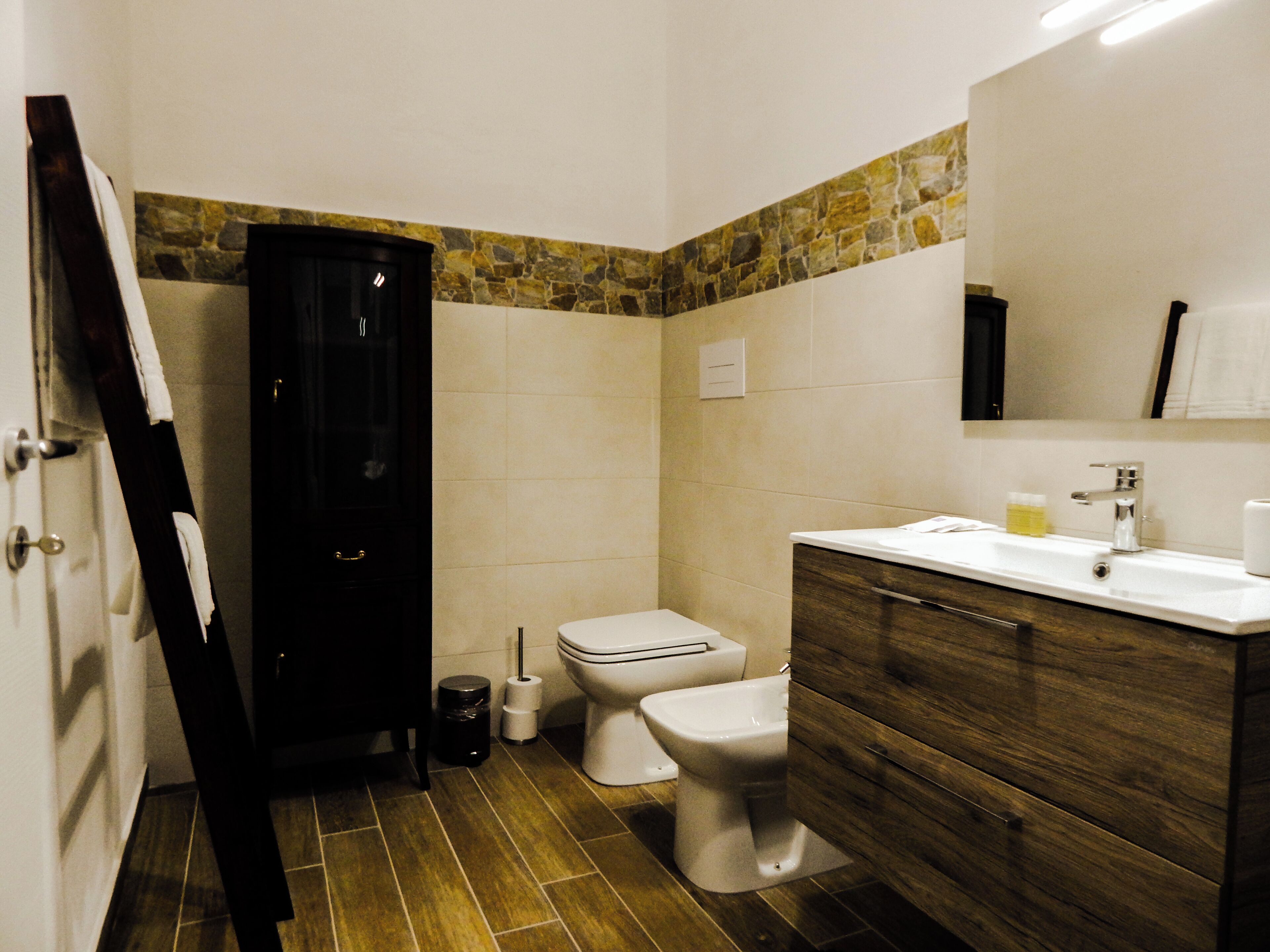 A bathroom with a toilet, bidet, and a wooden vanity with a mirror.
