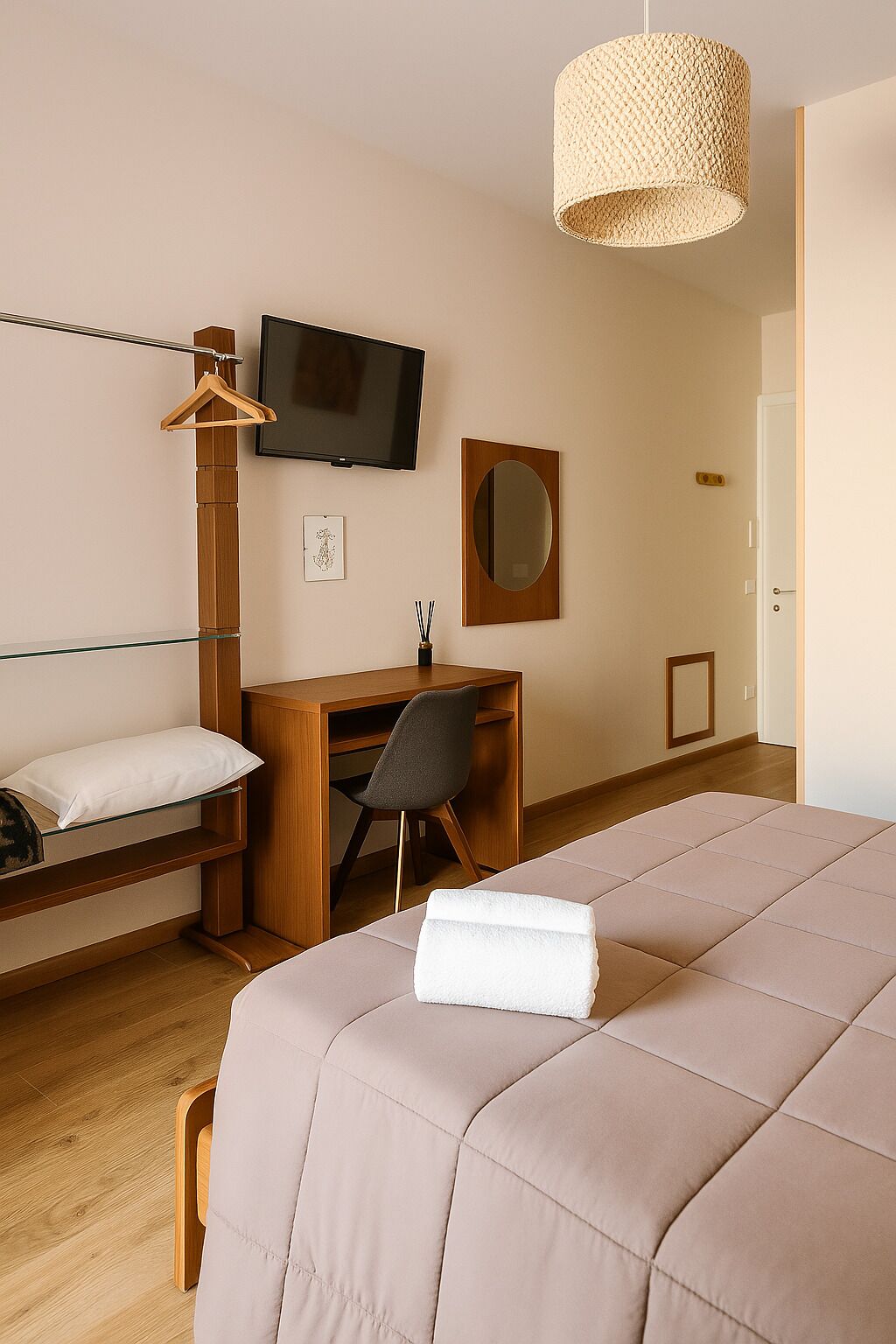 A modern hotel room with a bed, a desk, a chair, a television, and a hanging light fixture.