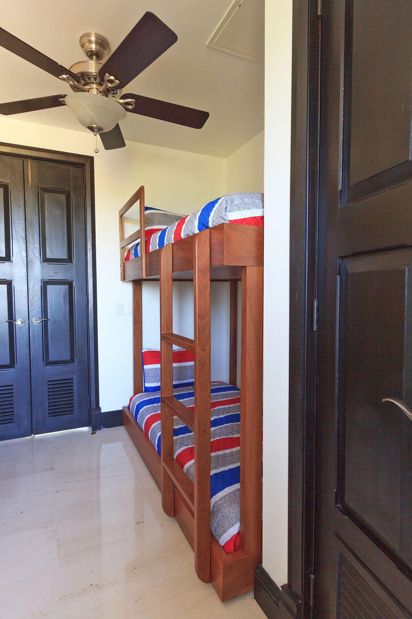 A room with a bunk bed, a ceiling fan, and a dark wooden door.