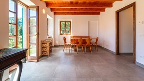 Amplia habitación con techo de madera, una mesa de comedor con sillas, un piano y una ventana con vista a la vegetación.