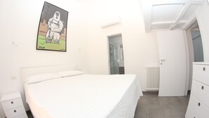 A bedroom with a bed, a white dresser, a radiator, and a door leading to a bathroom.