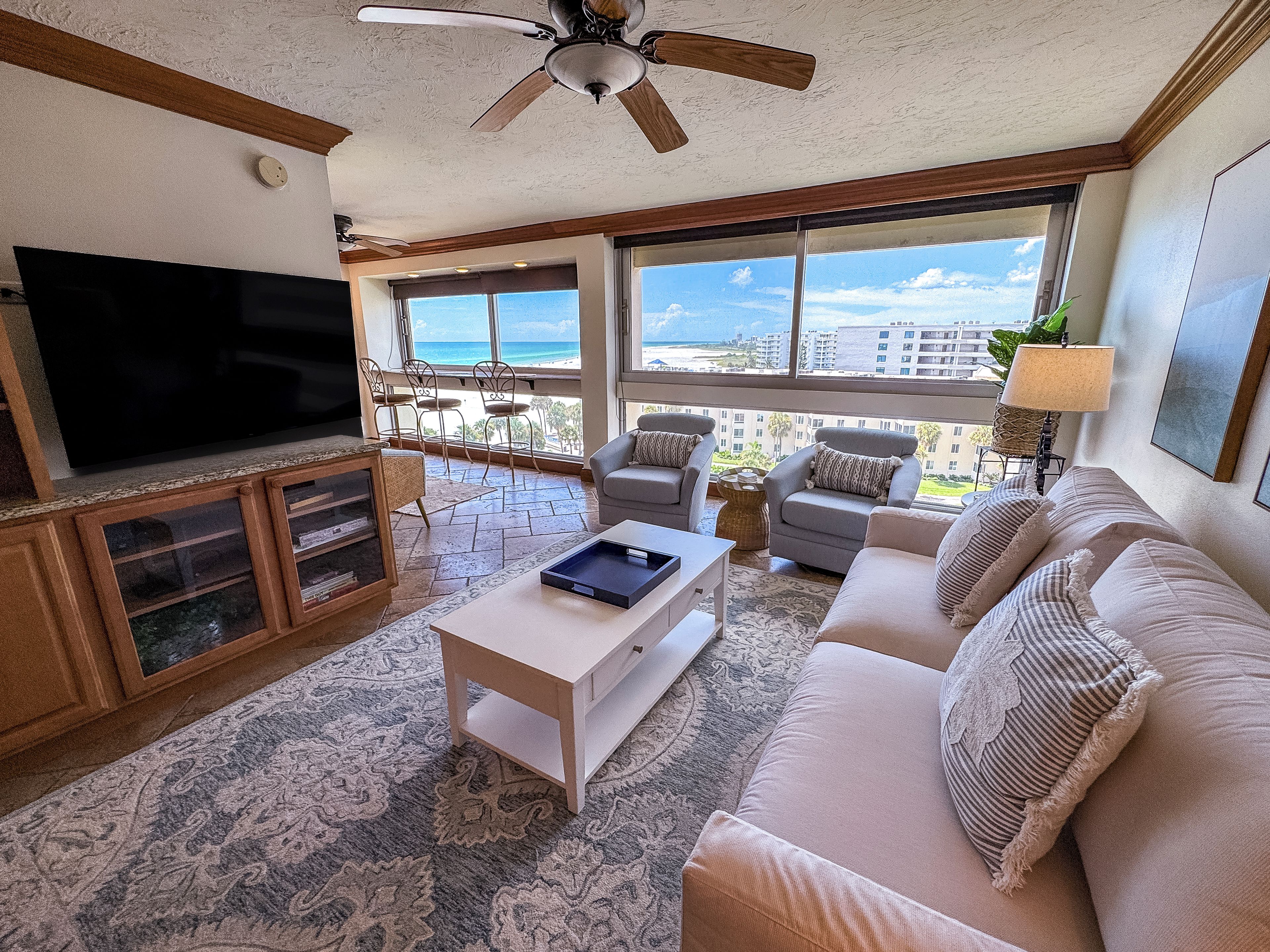 Ein Wohnzimmer mit Flachbildfernseher, Deckenventilator, einer Couch und Blick auf den Strand.