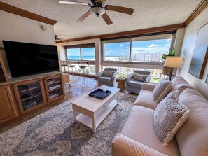 A living room with a flat-screen TV, a ceiling fan, a sofa, and a view of the beach. - Unit 84- 1 Bedroom 1 Bathroom Condominium with Partial North Views. (Sarasota)