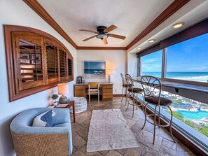 A room with a desk, chairs, a ceiling fan, a large window with a beach view, and a decorative wooden window frame. - Unit 84- 1 Bedroom 1 Bathroom Condominium with Partial North Views. (Sarasota)