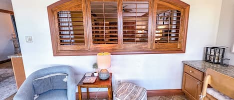 A room with a large arched window, a small table with a lamp, a chair, and a cabinet.