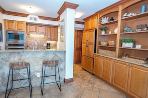 A kitchen with wooden cabinets, a built-in microwave, and a stone backsplash. - Unit 84- 1 Bedroom 1 Bathroom Condominium with Partial North Views. (Sarasota)