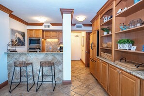 A kitchen with wooden cabinets, a granite countertop, two bar stools, and a tiled backsplash. - Unit 84- 1 Bedroom 1 Bathroom Condominium with Partial North Views. (Sarasota)