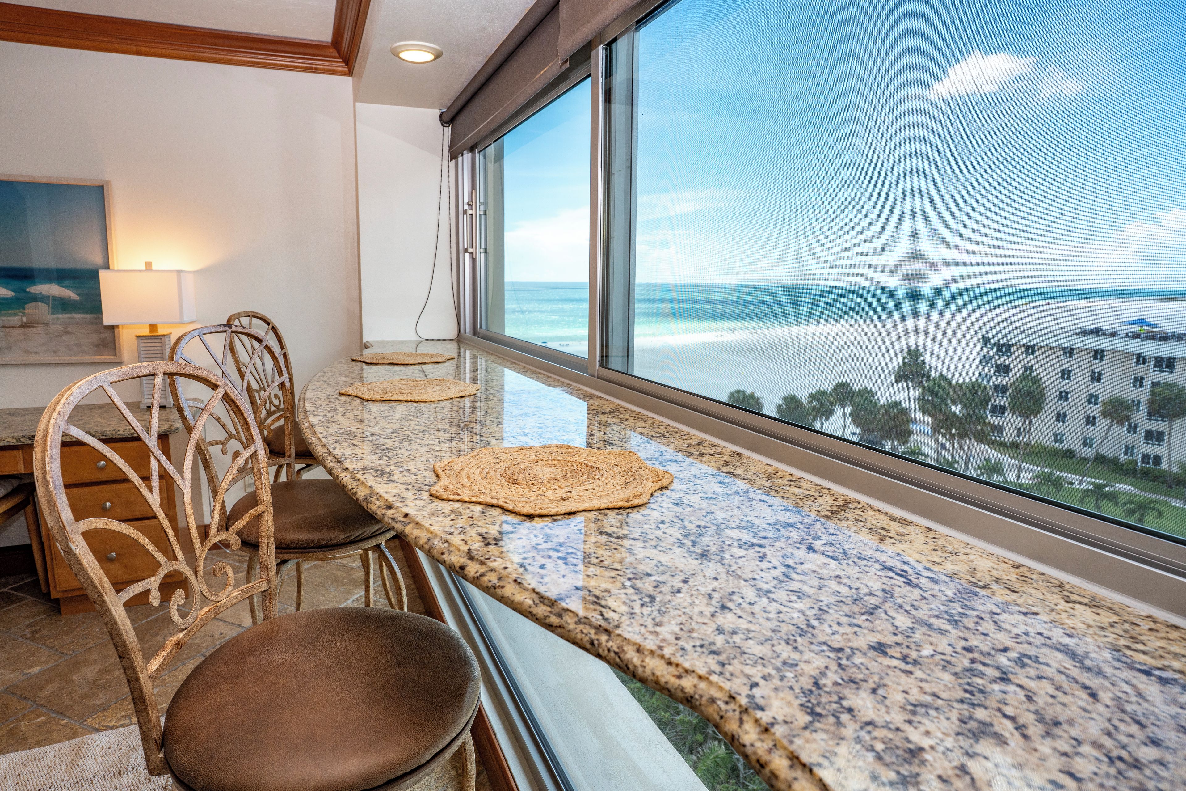 A dining area with a view of the ocean, a table with placemats, and a chair with a cushioned seat.