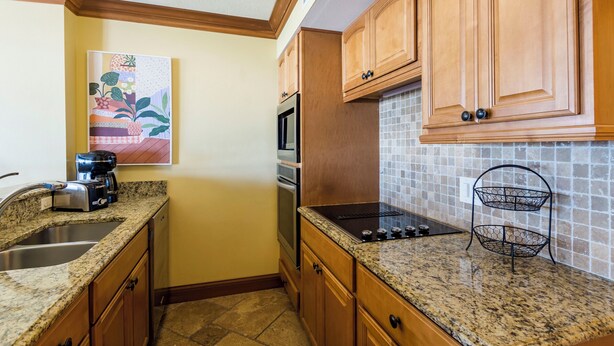 A kitchen with granite countertops, wooden cabinets, a stainless steel sink, a microwave, an oven, and a two-tiered wire basket. - Unit 84- 1 Bedroom 1 Bathroom Condominium with Partial North Views. (Sarasota)
