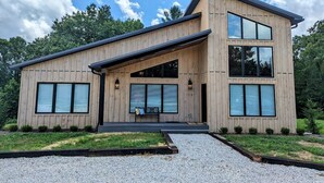 A modern two-story house with a wooden exterior, large windows, and a gravel driveway.