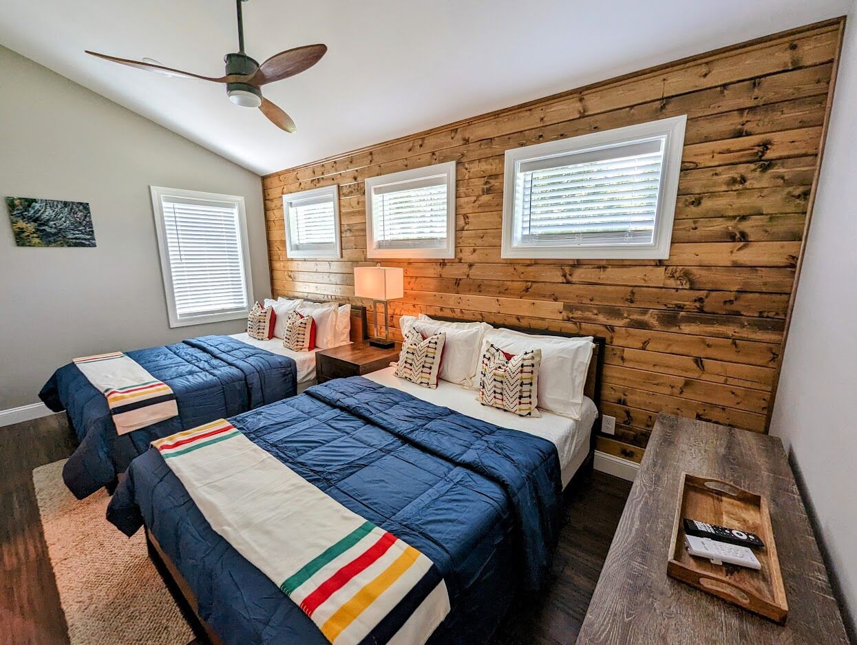 Ein Schlafzimmer mit zwei Betten, Holzwandverkleidung und einem Deckenventilator.