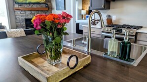 A wooden tray with a vase of flowers on a kitchen counter, a modern faucet, and two soap bottles.
