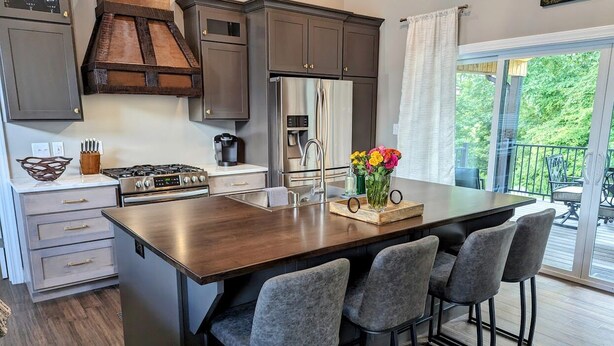 A modern kitchen with a central island, bar stools, and a view to an outdoor deck.