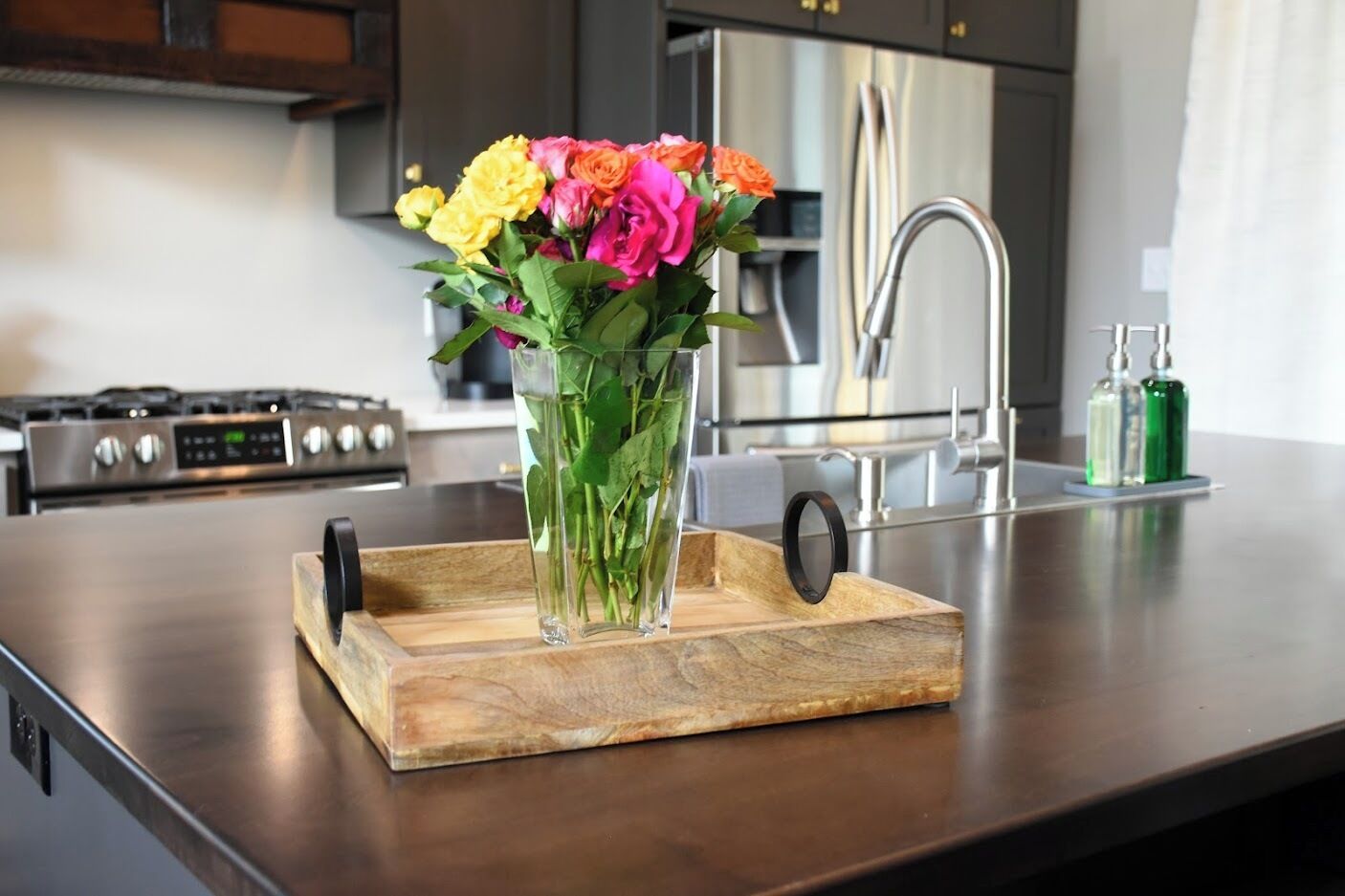 A kitchen counter with a wooden cutting board holding a vase of flowers.
