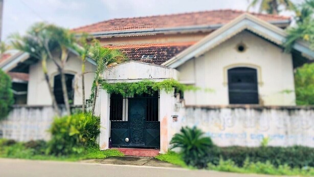 A two-story house with a tiled roof, a black door, and a small porch area with greenery.