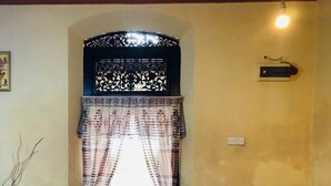 A room with a patterned chair, a small table with a vase, and a decorative wall hanging.