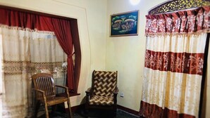A room with a wooden chair, a patterned armchair, and curtains with floral designs.