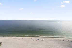 Une plage avec un ciel dégagé, une mer calme et plusieurs parasols de plage.