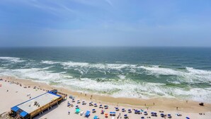 A beach with a lifeguard tower, umbrellas, and people. - Seawind 1604 by Liquid Life (Gulf Shores)