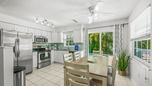 A modern kitchen with stainless steel appliances, a dining area with a table and chairs, and a view of a pool through large windows.