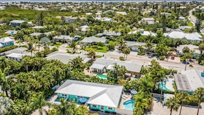 An aerial view of a residential area with houses, palm trees, and a swimming pool.