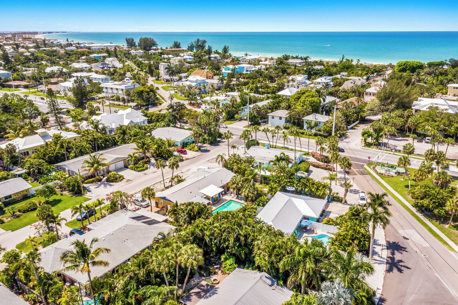 Vista aérea de una zona residencial costera con casas, palmeras y una vista despejada del océano.