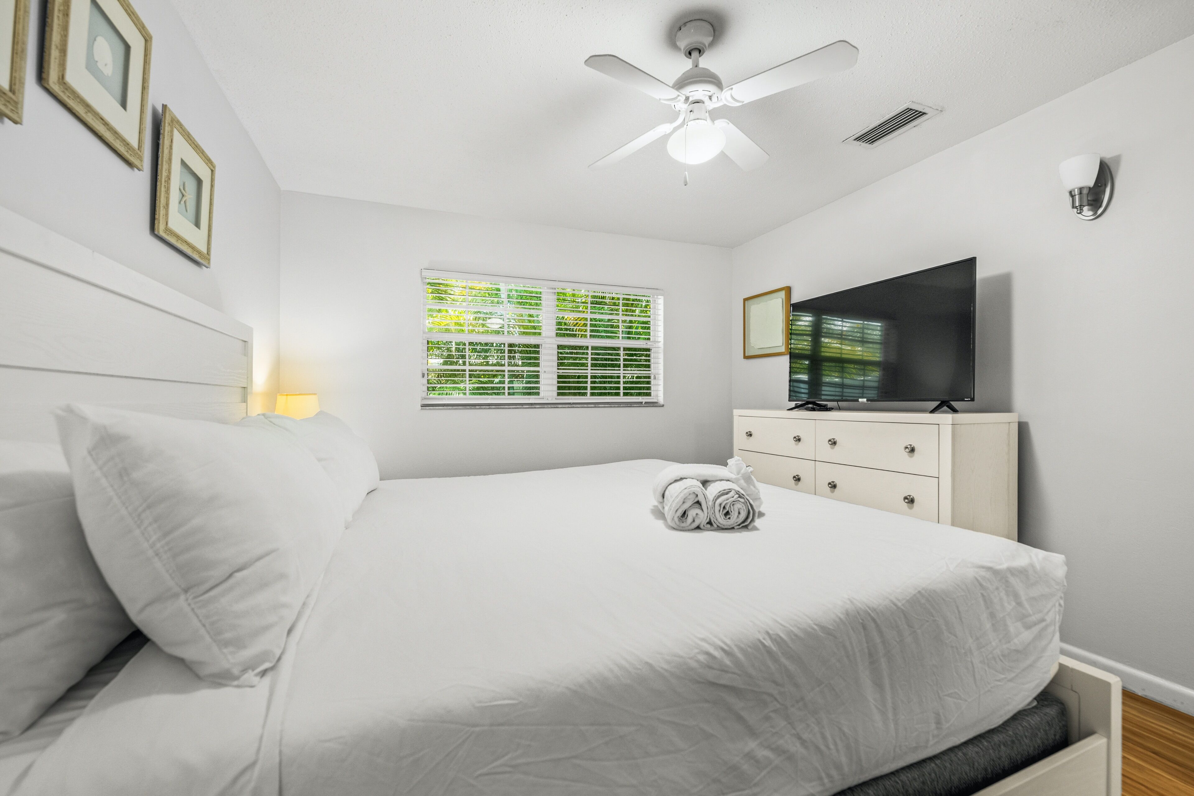 A bedroom with a bed, a TV, a ceiling fan, a window, and a dresser.