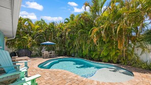 A swimming pool surrounded by palm trees and a patio area with chairs and a table.