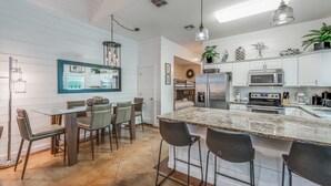 Una cocina moderna con armarios blancos, una isla de granito y taburetes de bar.