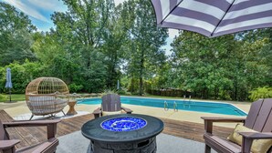 Um deck ao ar livre com lareira de pedra, cadeiras de descanso e piscina.