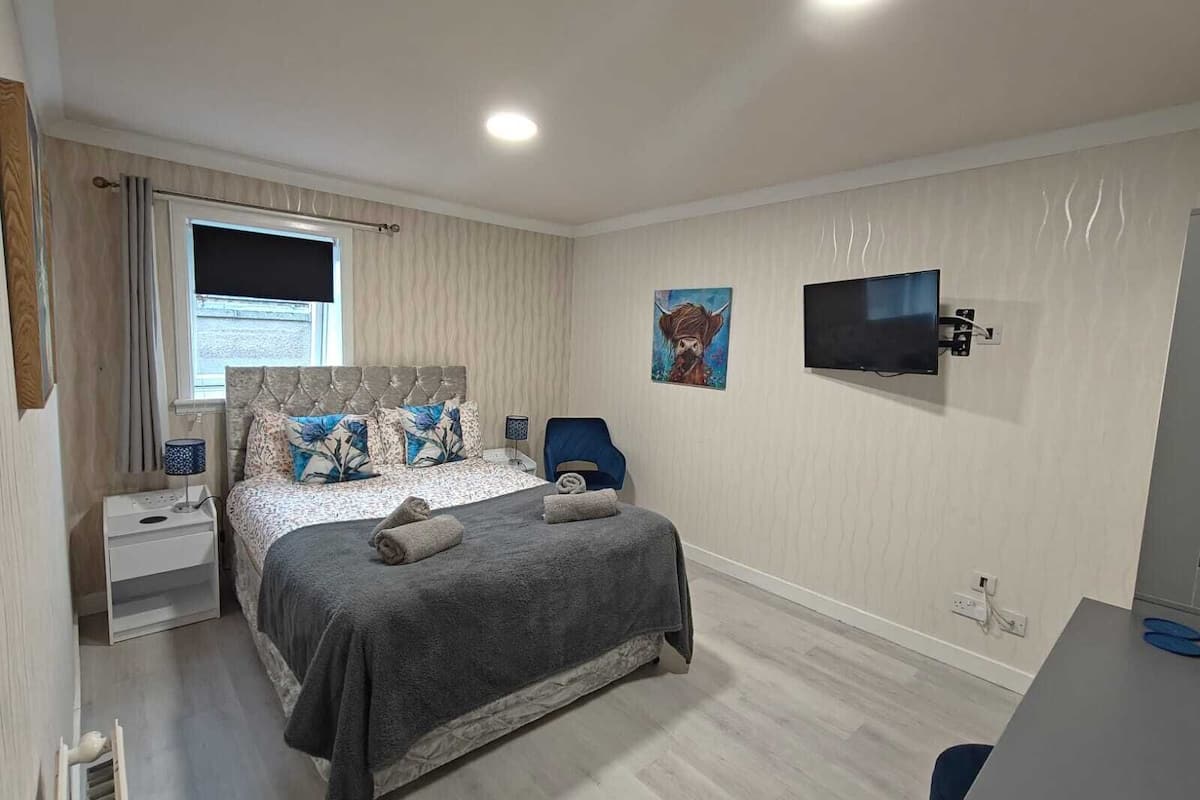 A bedroom with a bed, a TV, a painting, and a desk.