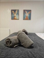 A room with a massage table, two rolled-up towels, and two paintings on the wall.