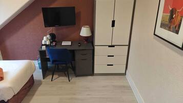 Habitació d'hotel amb llit, escriptori, cadira, televisió i armari.