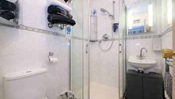 Un baño moderno con ducha envuelta en vidrio, inodoro, lavamanos y un perchero con toallas dobladas con cuidado.