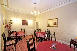 A dining area with two tables, red tablecloths, wooden chairs, a chandelier, and a floral wallpaper pattern. - The Jays Guest House (Aberdeen)