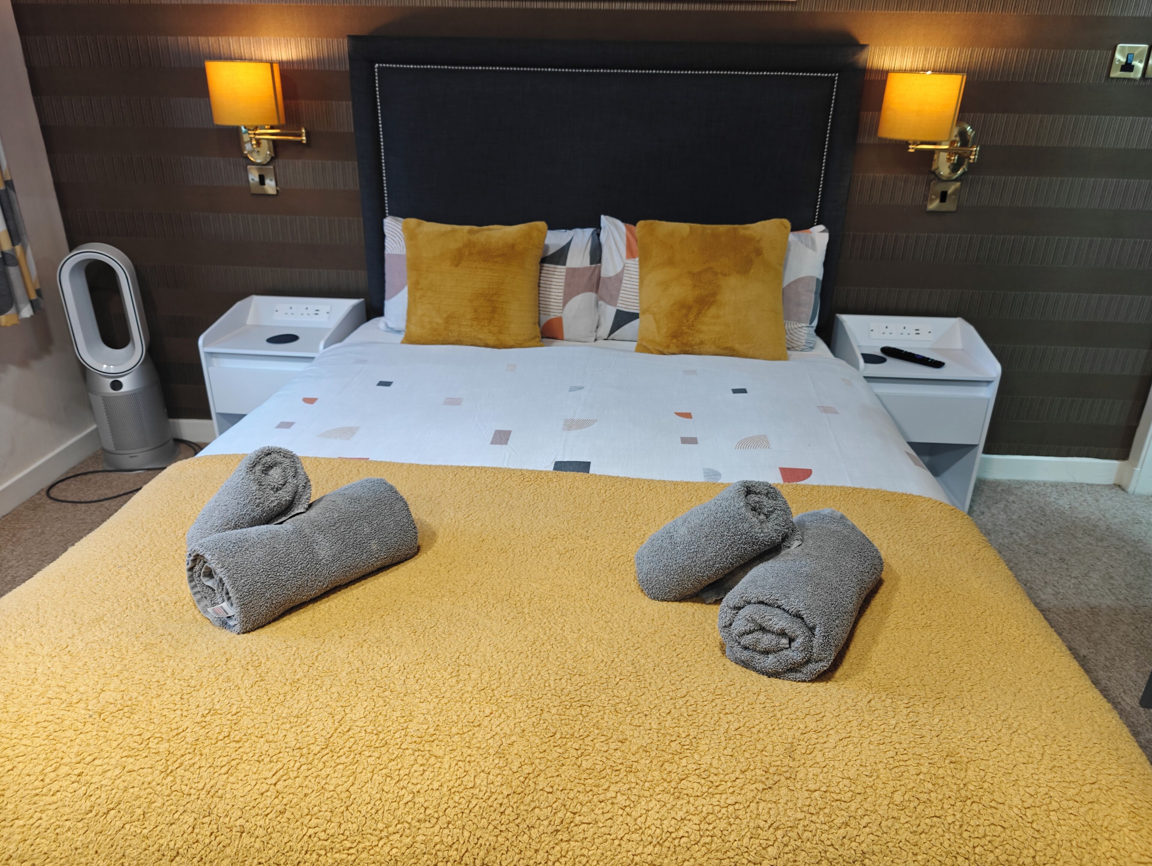 Une chambre d’hôtel avec un lit, deux tables de chevet, une lampe, un radiateur et des serviettes sur le lit.