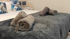 Ein ordentlich bezogenes Bett mit einer dunkelgrauen Decke und zwei aufgerollten Handtüchern darauf.
