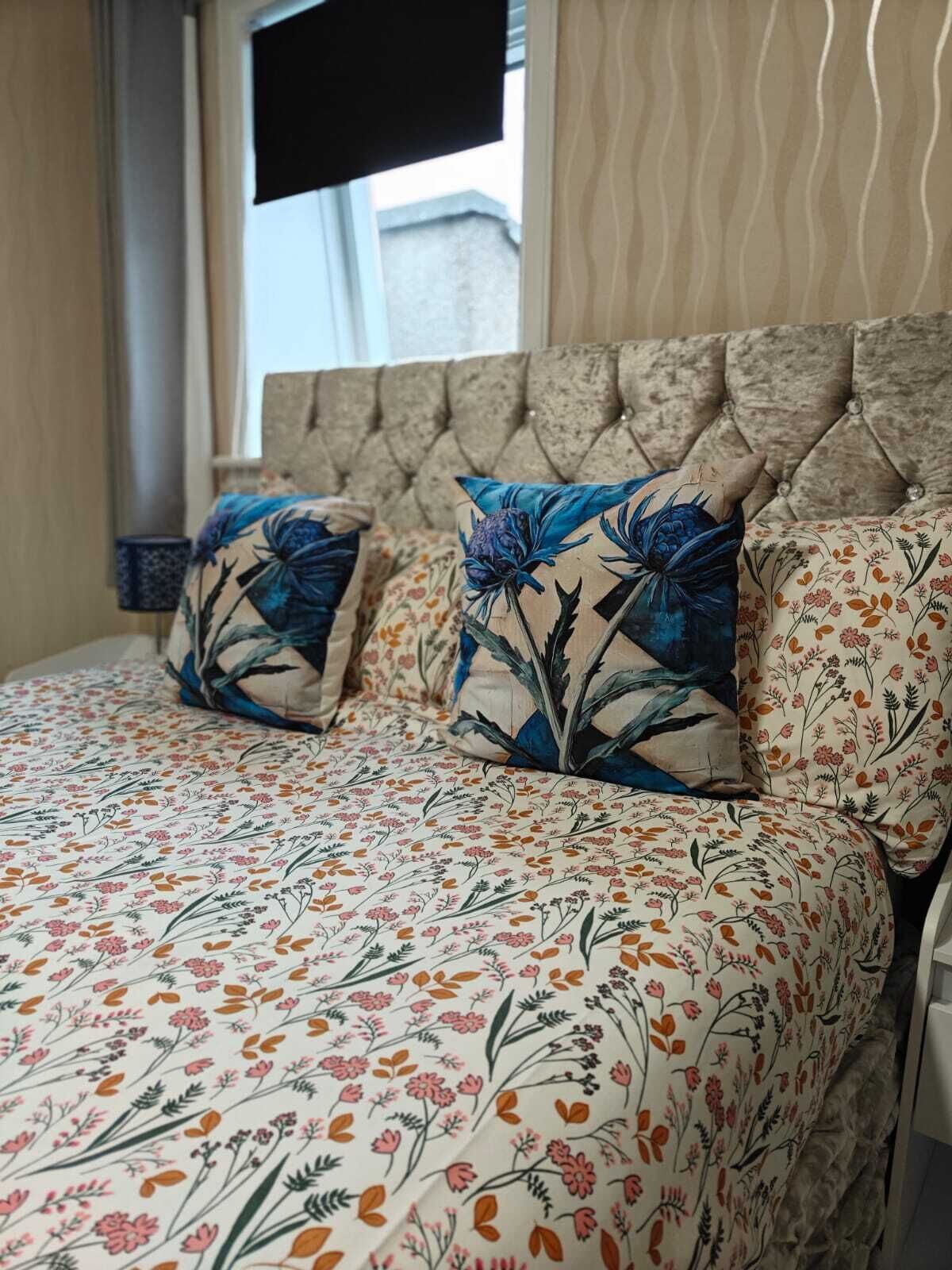 A bed with floral bedding and two decorative pillows, a tufted headboard, and a window with a view of the outside.